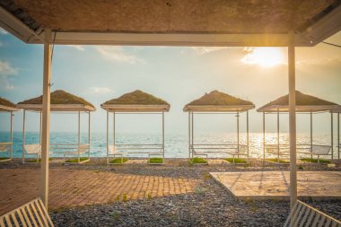 Kumsalda boş bir yazlık kafe. Salgın ve covid-19 nedeniyle ziyaretçi yok. Kanopi üzerinde masalar, ahşap döşemeler. Sahil şeridinde deniz manzaralı bir restoran. Kapalı sınırlar, turist eksikliği. İyi akşamlar. Güneş