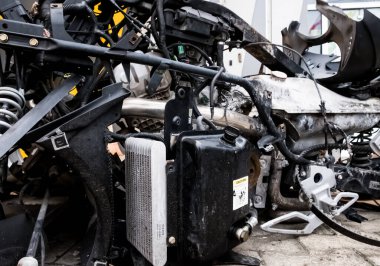 Araç, üç tekerlekli bisiklet, kazadan sonra. Atölyenin yanında yanmış bir motosiklet. Küle bulanmış mekanizma metali. Çeşitli motosiklet mekanizmaları görünür. Dişliler, yaylar, tanklar, iskelet, traksiyon.