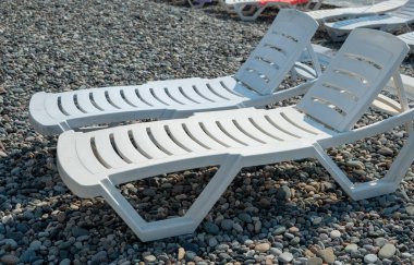 Plajda beyaz plastik güneş panjurları. Çakıl taşlı deniz kıyısı. Boş plaj sandalyeleri. İyi günler. Yaz. Georgia.