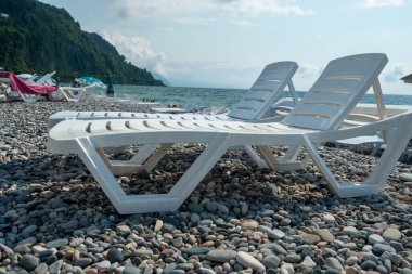 Plajda beyaz plastik güneş panjurları. Çakıl taşlı deniz kıyısı. Boş plaj sandalyeleri. İyi günler. Yaz. Georgia.