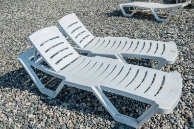 Plajda beyaz plastik güneş panjurları. Çakıl taşlı deniz kıyısı. Boş plaj sandalyeleri. İyi günler. Yaz. Georgia.