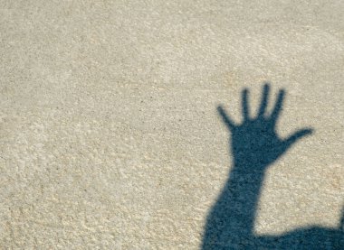 Beton zeminde şapkalı bir adamın gölgesi. İnsan elleri, gölgeden gelen karanlık siluetleri gösterir. Tamam, beş, işte, zafer. İyi günler. Güneşli. Georgia.