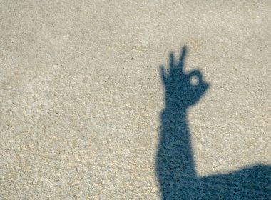 Beton zeminde şapkalı bir adamın gölgesi. İnsan elleri, gölgeden gelen karanlık siluetleri gösterir. Tamam, beş, işte, zafer. İyi günler. Güneşli. Georgia.