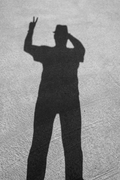 Shadow of a man in a hat on the concrete floor. Human hands show symbols Dark silhouette from shadow. Signs: Okay, five, there, victory. Day. Sunny. Georgia.