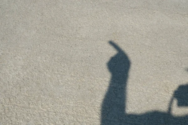 Shadow of a man in a hat on the concrete floor. Human hands show symbols Dark silhouette from shadow. Signs: Okay, five, there, victory. Day. Sunny. Georgia.