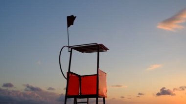 Deniz kenarındaki kurtarma kulesi. Suyun yanındaki kırmızı gözlem noktası. İşaret, kırmızı bayrak. Rüzgar kırmızı bayrağı dalgalandırıyor. Sancak rüzgardan titriyor. Georgia mı? İyi günler, güneşli. Yaz.