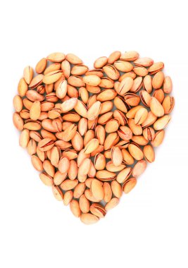 Organik fıstıklar beyaz arka planda izole edilmiş kalp şekli oluşturuyor. İçerisi kırmızı.