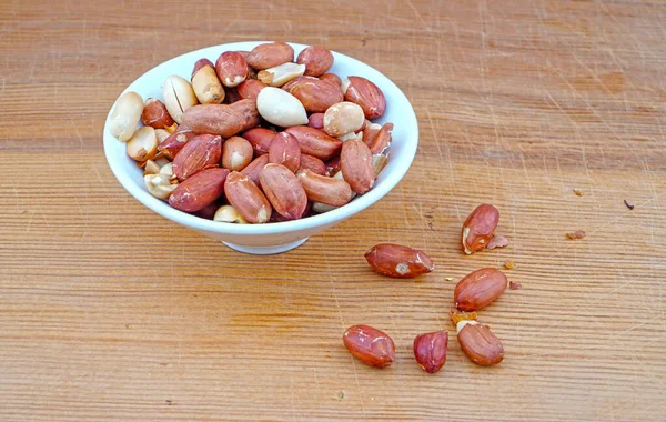 Platful Organic Ungesalzene Erdnüsse Und Verschüttete Ungesalzene Erdnüsse Auf Holz — Stockfoto