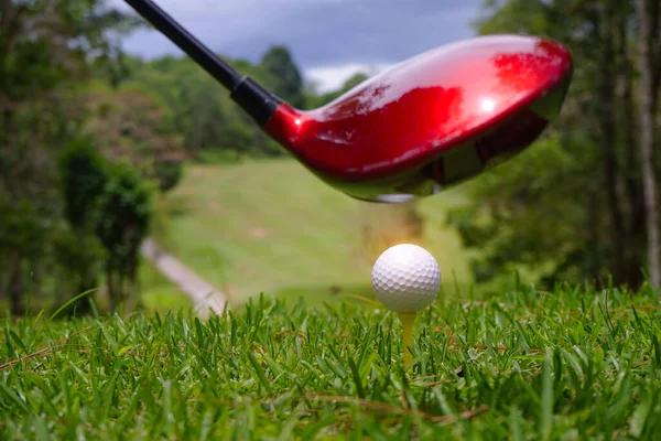 Golf ball and blurred golf club in the beautiful golf course in Thailand. Collection of golf equipment resting on green grass with green background.