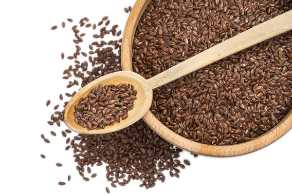 Close up of linseeds or flax seeds in wooden spoon on top of a wooden bowl with some spread on the blurred white background seen from above