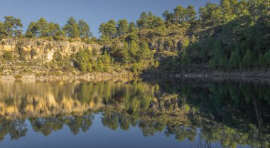 Lagün içinde yansıyan kayalar ve ağaçlarla çevrili.