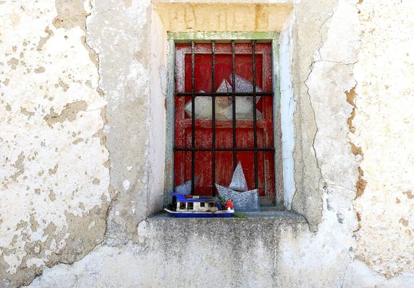 Beyaz bir duvarda siyah çubuklar ve kırmızı panjurlar ile Rustik pencere. 