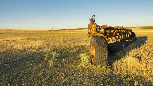 Hasat edilen bir yaz tarlası üzerinde terk edilmiş eski ve paslı tarım makineleri.