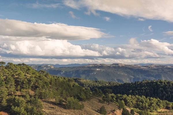 Mavi gökyüzü ve beyaz bulutlar altında dağlık ve engebeli manzara.