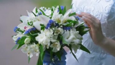 Gelin elinde büyük bir güzel düğün buketi tutuyor, içinde çiçekler dokunmadan, parmaklarıyla onları parmaklama
