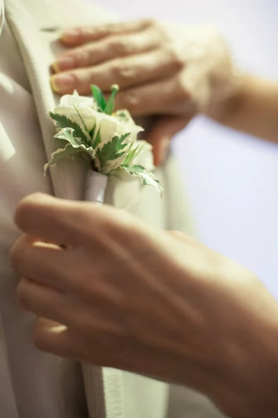 Mãos de noivas vai endireitar o botão na lapela do casaco de noivos — Fotografia de Stock