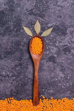 Düzgün beslenme için çiğ portakallı mercimek ve gri arka planda defne yaprakları olan ağaç şeklinde bir tahta kaşıkta vejetaryenlerin sağlığı.