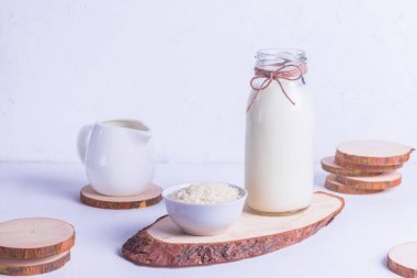 Bardak şişesinde vejetaryen pirinç sütü ve beyaz arka planda beyaz bir tabakta pirinç.