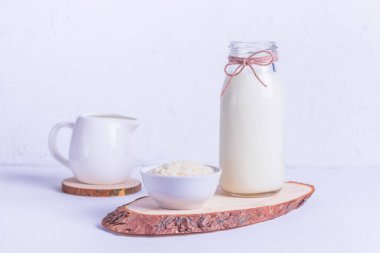 Bardak şişesinde vejetaryen pirinç sütü ve beyaz arka planda beyaz bir tabakta pirinç.