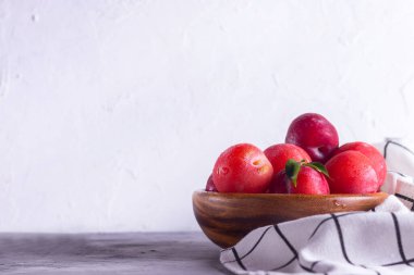 Ahşap bir tabakta olgun erikler, yüksek tuşlu gri bir arka planda bir peçeteyle çiğ tanesiyle.