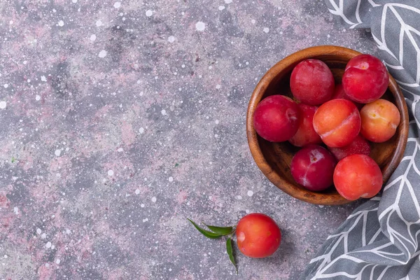 Ripe plums in a wooden plate with a tissue napkin on a gray background