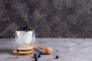 Naneli Chia pudingi ve bardaklı yaban mersini. Koyu arkaplanda bal çubuğu olan ahşap bir stantta.