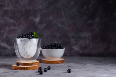 Naneli Chia pudingi ve bardaklı yaban mersini. Gri arka planda bir tabak yaban mersini ile ahşap bir stantta.