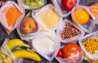 Mısır gevrekleri, meyveler ve sebzeler karanlık bir masada plastik torbalarda.