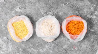 Millet, pirinç ve turuncu mercimek gri arka planda plastik torbalarda