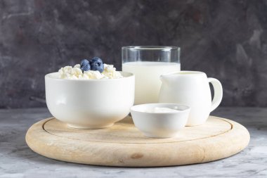 Ekşi krema, krema ve sütle kaplı beyaz tabakta, gri arka planda tahıllı süzme peynir.