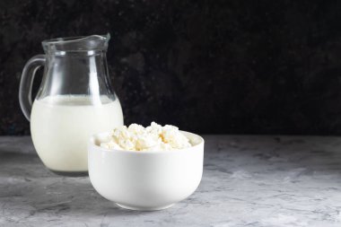 Koyu arkaplanda süt sürahisi olan beyaz tabakta süzme peynir.