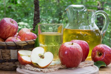 Açık havada bir cam ve sürahi elma suyu ve taze kırmızı elma rustik ahşap yüzeyi ile