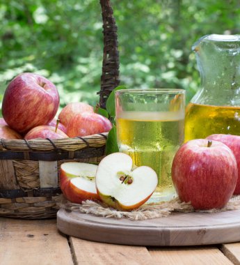 Açık havada bir cam ve sürahi elma suyu ve taze kırmızı elma rustik ahşap yüzeyi ile