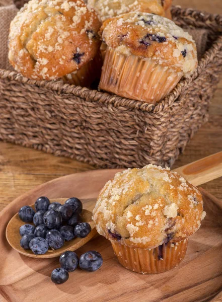 Blueberry muffins and spoonful of berries on a wooden plate with basket of muffins in background