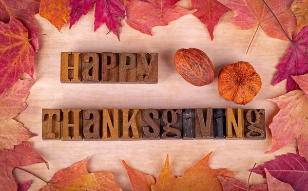 Happy Thanksgiving text written with wooden block letters surrounded by a colorful autumn leaf border