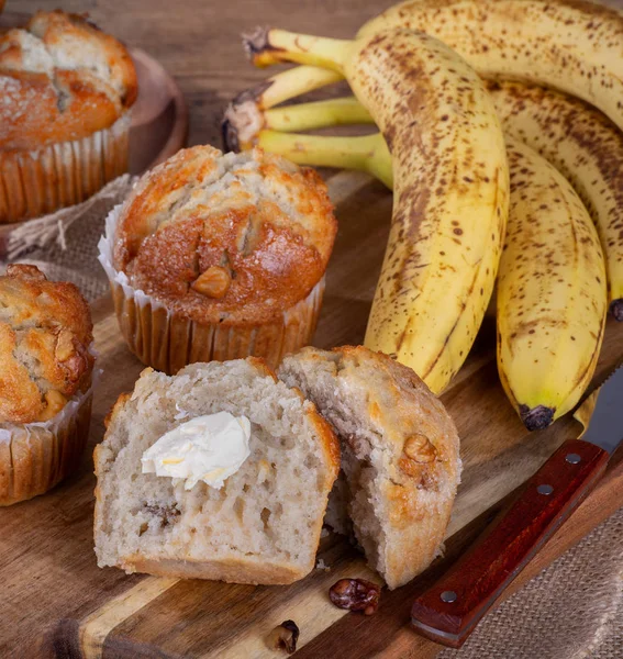 Banana nut muffin cut in half with butter and bananas in background