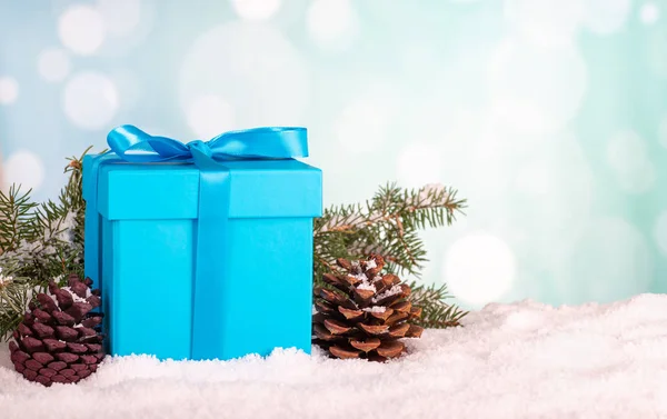 Blue Christmas gift box with pine cones and evergreen tree branches on snow against a colorful bright background