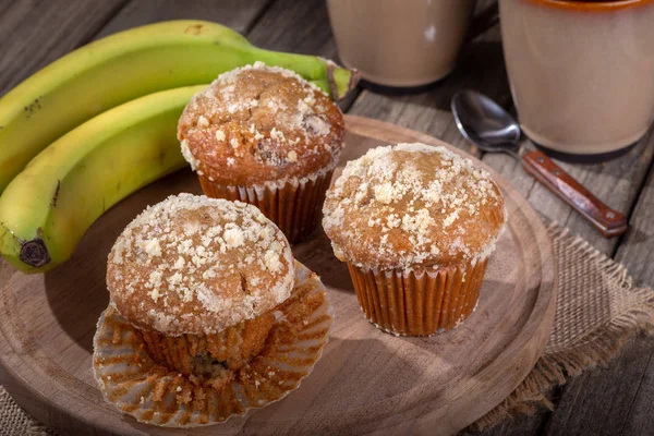 Banana nut muffins and bananas on a wooden tray with coffee cups in background
