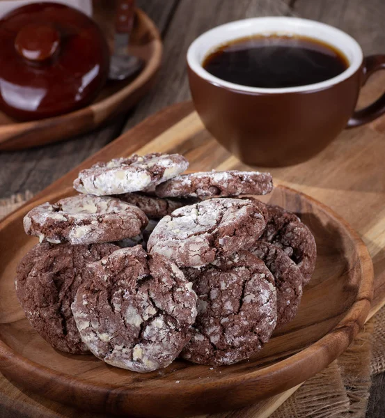 Chocolate fudge cookies on a rustic wooden plate with steaming cup of coffee in background