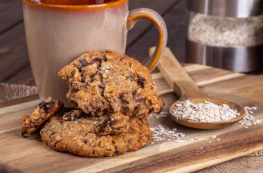 Yulaf ezmesi kuru üzüm fındık kurabiyeleri ve yulaf gevreği bir fincan kahve ile bir ahşap yüzeye