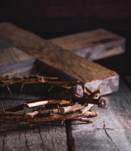 Crown of thorns and nails on a rustic wooden surface with a wood cross in background