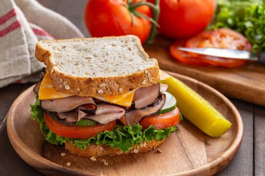 Jambonlu ve peynirli sandviçe yakın, marul, domates ve salatalıklı tahıllı ekmek ve ahşap tabakta.