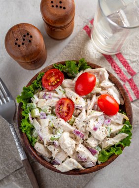 Chicken salad with lettuce and grape tomatoes in a wooden bowl.  Overhead view on a table with drink and salt pepper shakers clipart