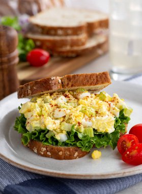 Tam tahıllı ekmek ve tabakta üzüm domatesli marullu yumurta salatalı sandviç. İçecek ve ekmek dilimleriyle bulanık arkaplan