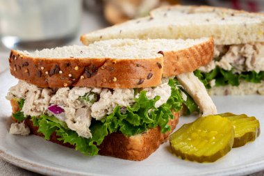 Ton balığı salatası ve marullu sandviç. Beyaz tabakta dilimlenmiş turşu ve çoklu tohum ekmeği.