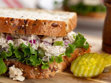 Ton balığı salatası ve çoklu tohum ekmeğinde marullu sandviç ve tahta tahtada dilimlenmiş turşu.