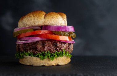 Salatalı, domatesli, turşulu ve soğanlı ızgara hamberger. Koyu renkli bir arka planda, fotokopi alanı olan tam tahıllı çörek.