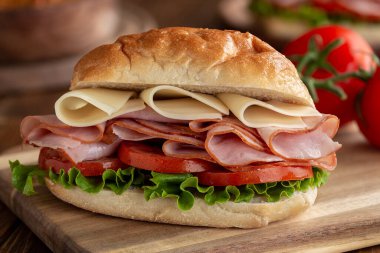 Salamlı ve peynirli sandviç, salatalı ve domatesli tahta üzerinde ekmek.