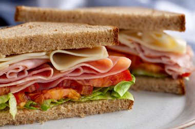 Jambonlu sandviç, peynirli, marullu ve domatesli tam buğdaylı ekmek tabakta ikiye bölünmüş.