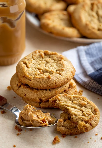 Peanut butter cookies on a table with peanut butter jar and plate of cookies in background